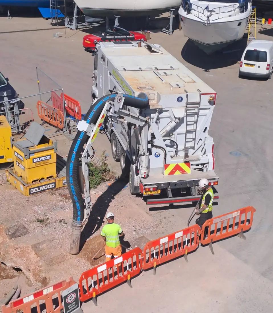 Vacuum excavator hose working in a fenced excavation on a marina site